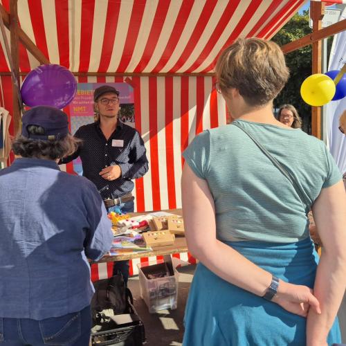 Ein Mann steht mit mehreren Menschen an einem bunten Marktstand